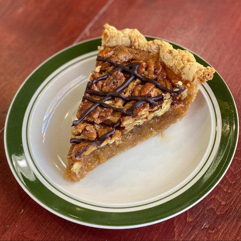 A slice of Bourbon Chocolate Pecan Pie on a plate with a flaky crust and chocolate drizzle.