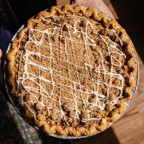 Pie with a crumbly crust and white drizzle held by a person
