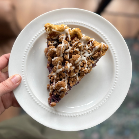 Slice of blueberry muffin pie on a white plate held by a person.