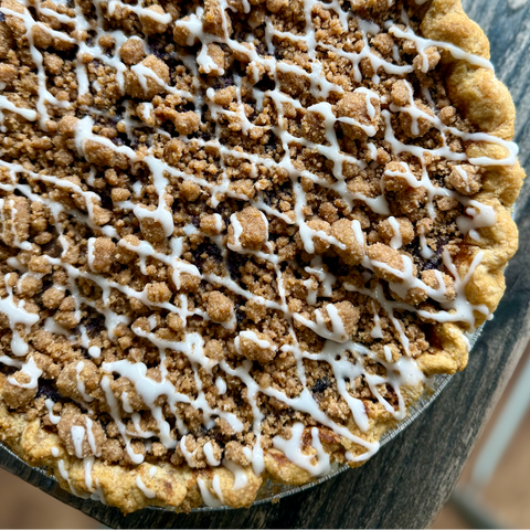 Close-up of a crumbly pie with white drizzle on a wooden surface