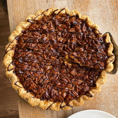 Whole Pie of Bourbon Chocolate Pecan Pie with slice being removed and white plate in image