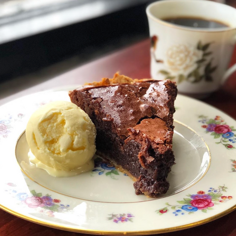 Slice of chocolate cake with vanilla ice cream on a floral plate, accompanied by a cup of coffee.