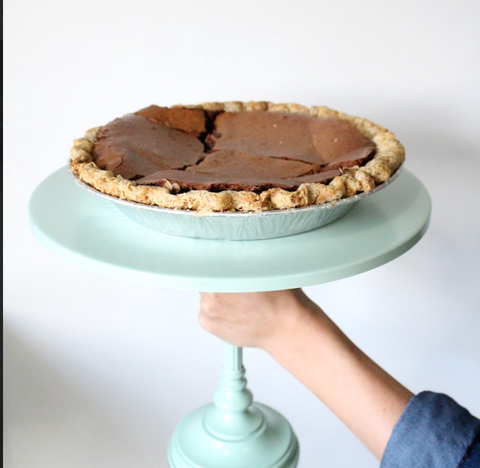 Chocolate pie on a light blue cake stand held by a person